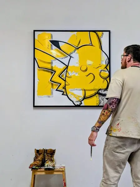 The Yellow Starter by Remco, a square yellow mixed media painting on a white wall, with the artist standing beside it holding a brush